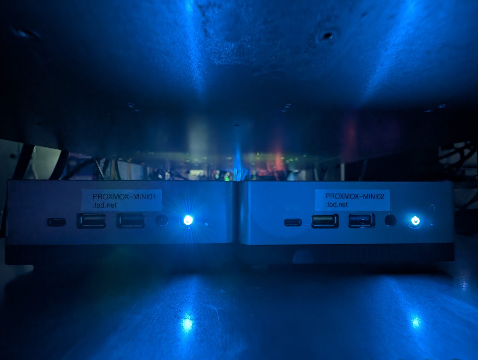 Two Minisforum mini PCs side by side, front panels labelled PROXMOX-MINI01.tod.net and PROXMOX-MINI02.tod.net, blue power lights lit.