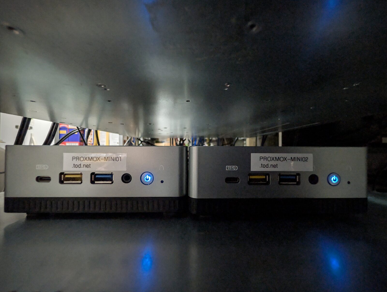 Two Minisforum mini PCs side by side, front panels labelled PROXMOX-MINI01.tod.net and PROXMOX-MINI02.tod.net, blue power lights lit.
