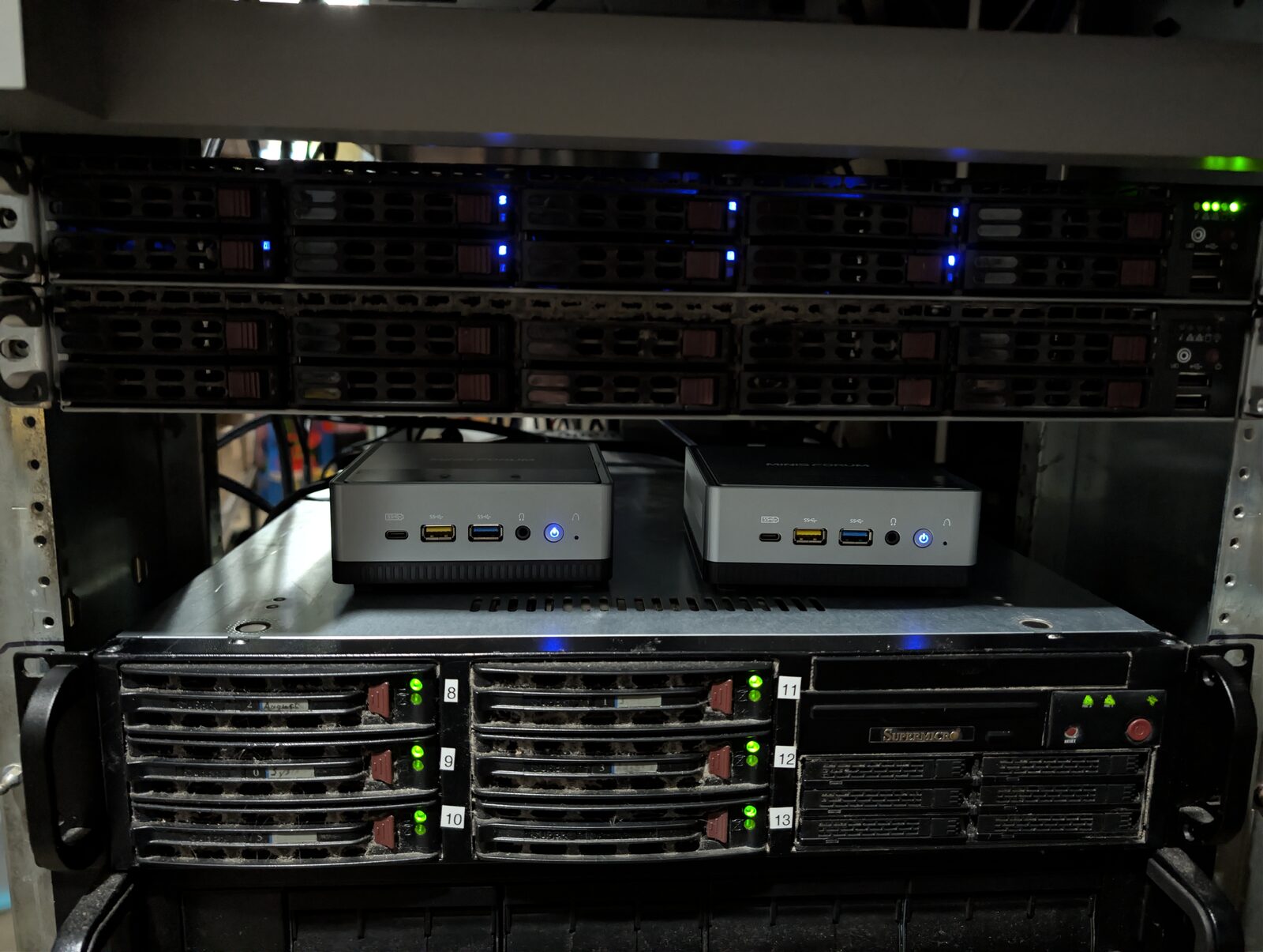 A stack of home server hardware: two 1U rackmount servers on top, two small mini PCs side by side in the middle, and a larger NAS chassis at the bottom.